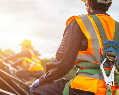 Two workers look to a hopeful sunrise as they work safely on a roof. 