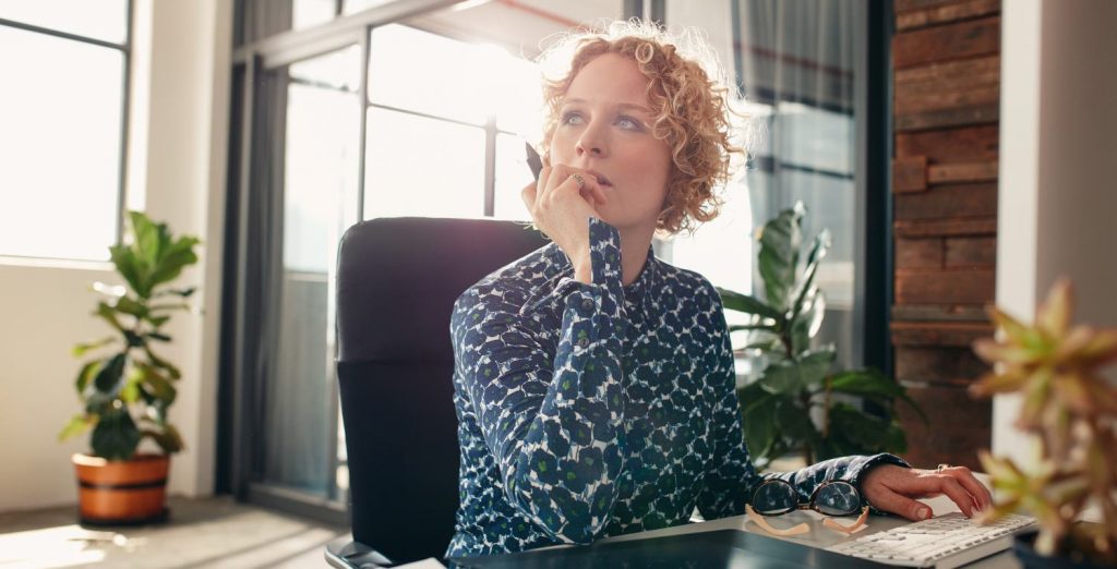 Portrait of young female designer sitting at her desk looking away and thinking.