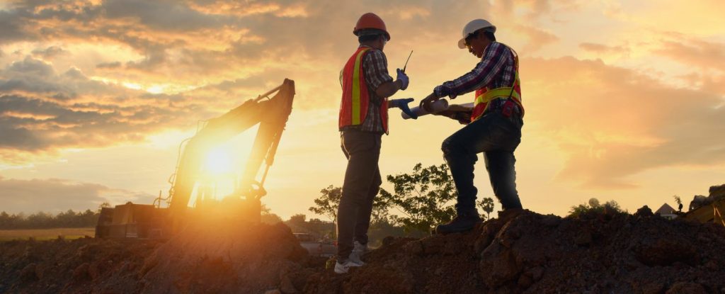 Engineers are working on road construction. engineer holdingradio communication at road construction site with roller compactor working dust road on during sunset