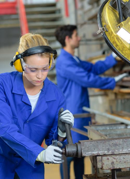 Female specialist cutting pipe using a bandsaw that creates noise hazard.