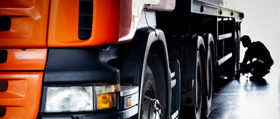 Silhouetted man checks beautiful orange truck tires during a pre trip inspection. 