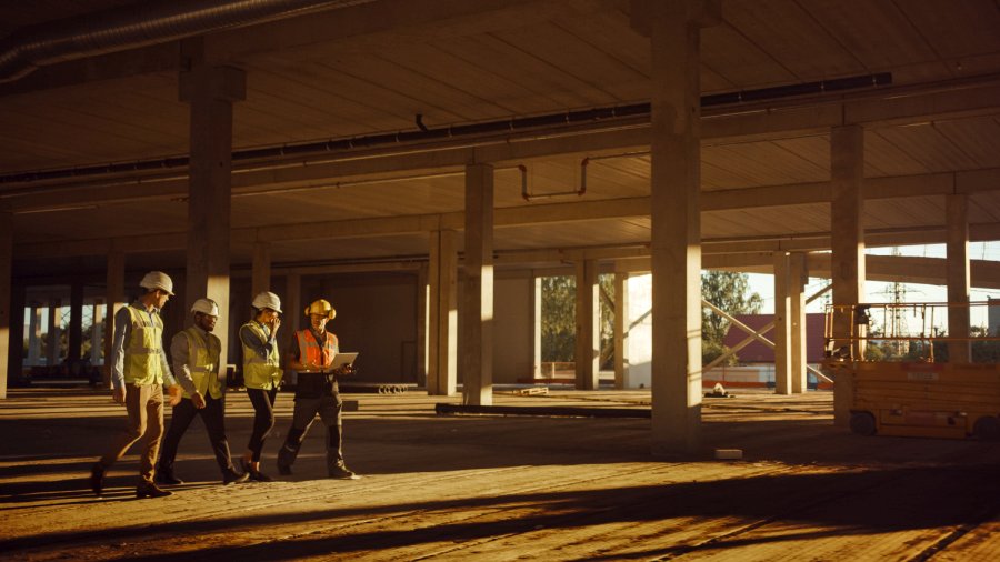 Diverse Team of Specialists Walk Through Garage Level of Industrial / Commercial Building Construction Site Discussing a toolbox talk. 